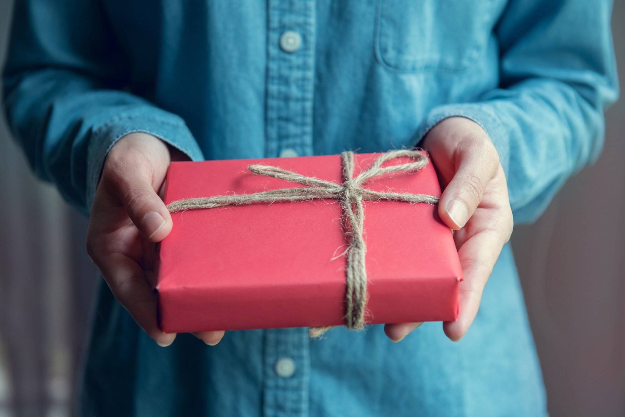 Giving a gift, Woman hands holding handmade present wrapped in red paper.