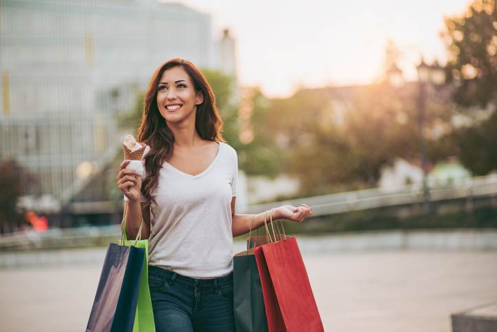 Young woman with shopping bags eating ice cream outdoors