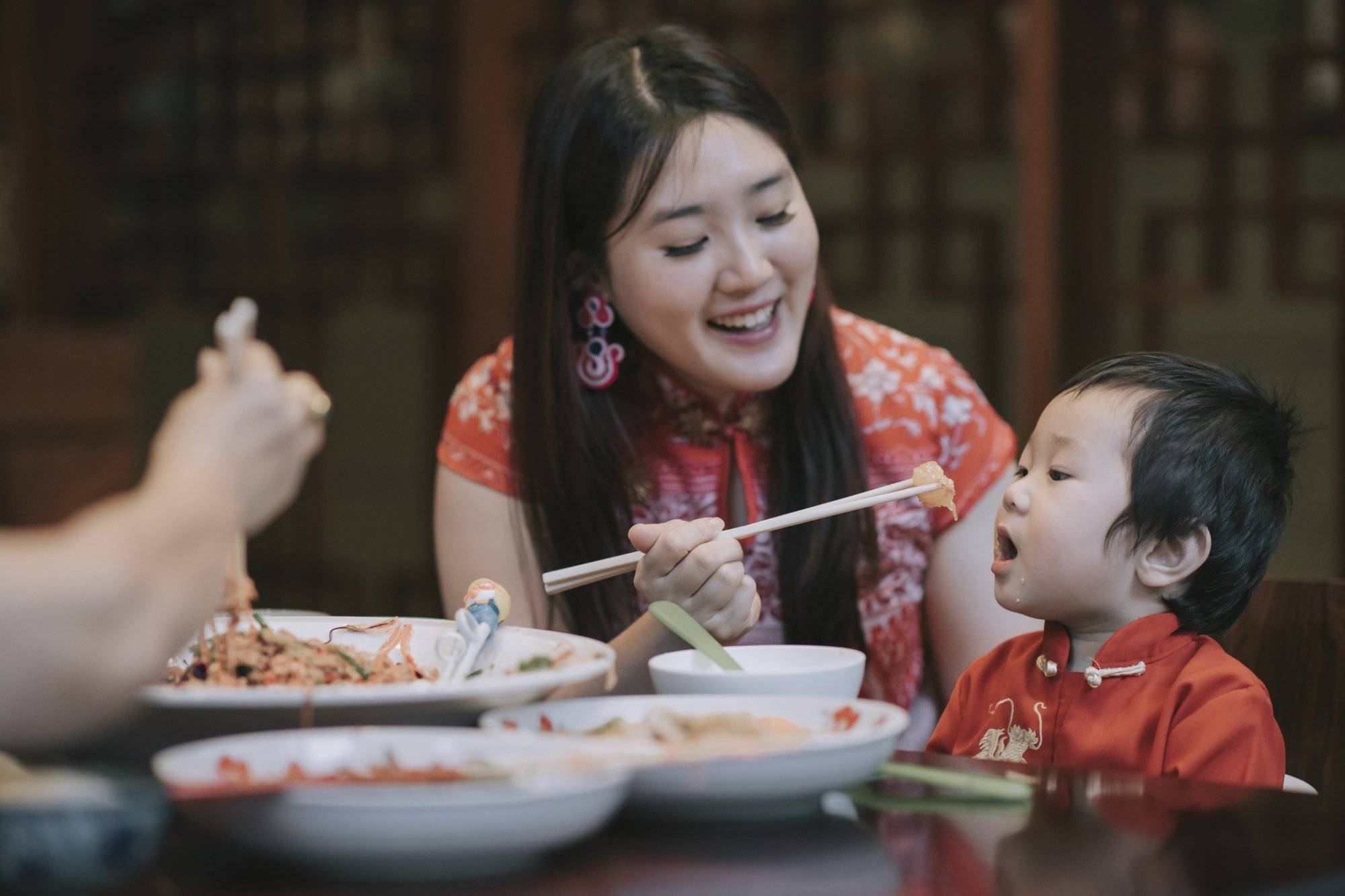 asian chinese mother feeding her son during family chinese new year reunion dinner with traditional dishes raw fish lau sang