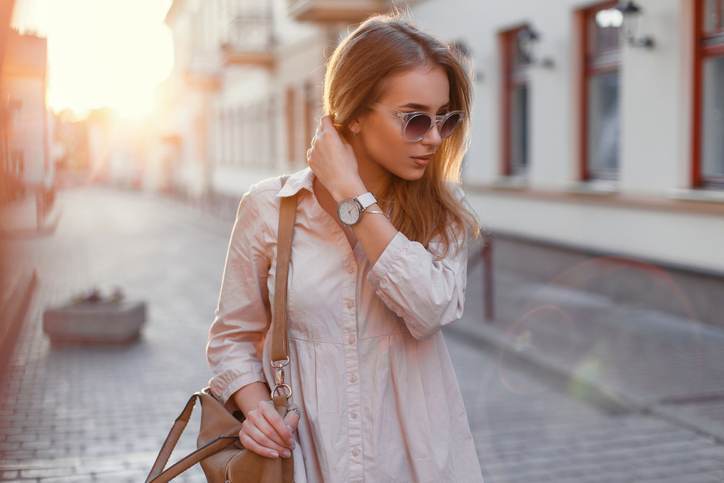 Beautiful girl in stylish sunglasses and with bag at sunset.