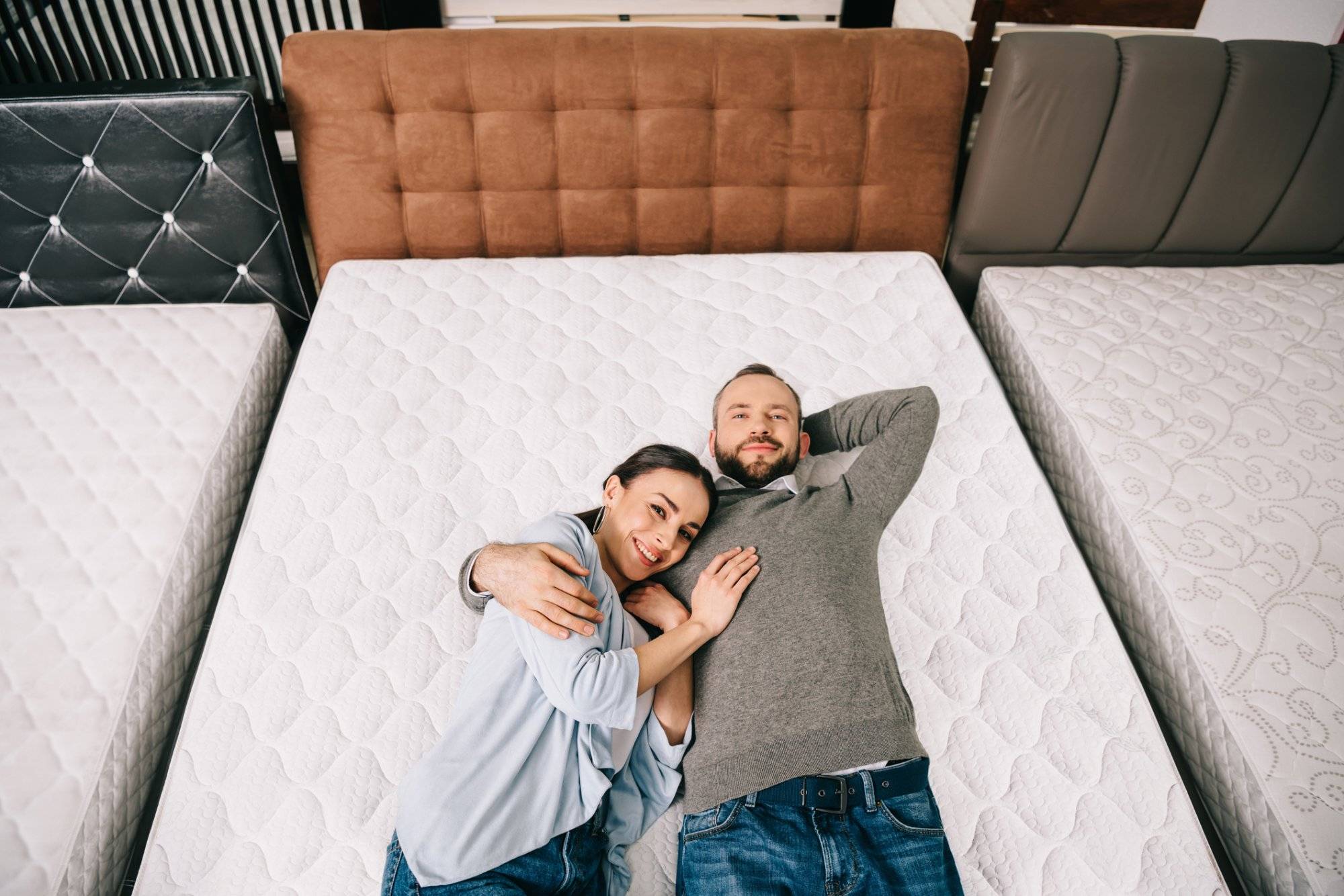 overhead view of smiling couple lying on bed in furniture store with arranged mattresses