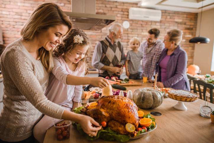 Happy mother and daughter preparing roasted turkey for Thanksgiving dinner.